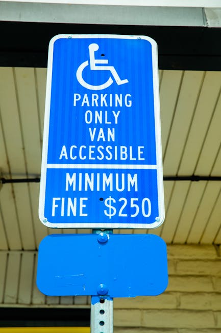 A blue parking sign with a white wheelchair symbol indicating accessible parking only for vans, attached to a metal pole beneath a building's overhang. The sign states 'PARKING ONLY VAN ACCESSIBLE' an